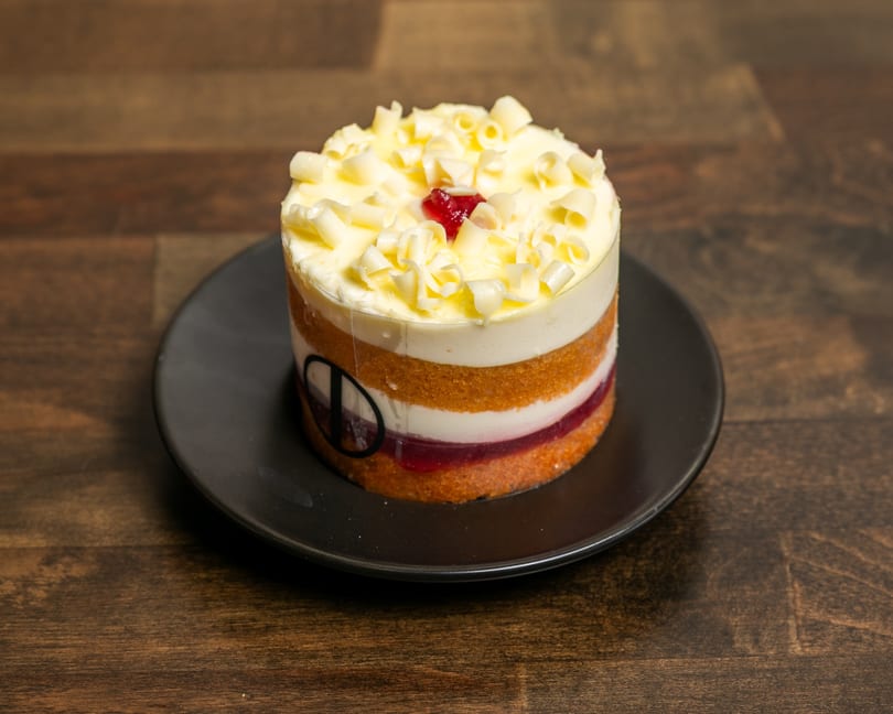 Layered dessert with white chocolate curls and a red jelly center on a black plate.