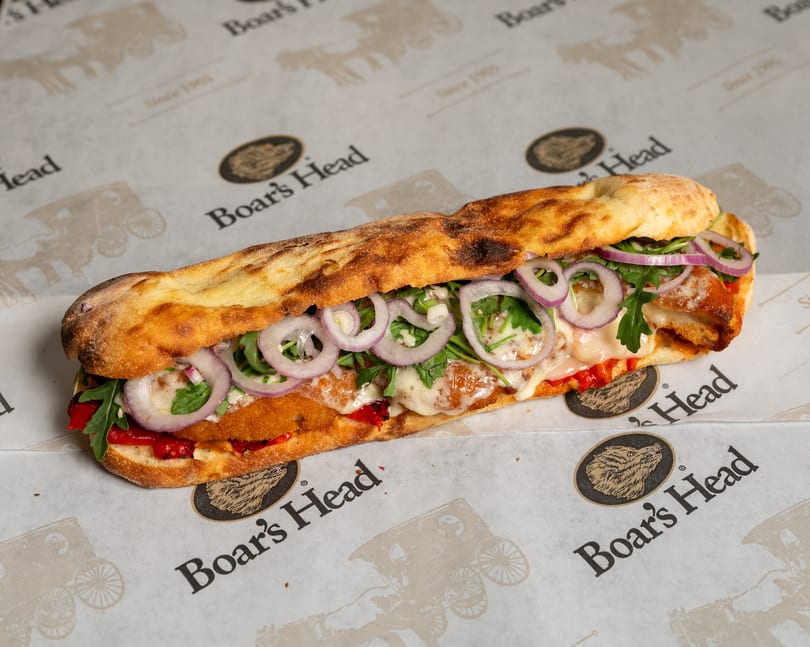 A Boar's Head sandwich with crispy chicken, melted cheese, red onions, and arugula on flatbread.